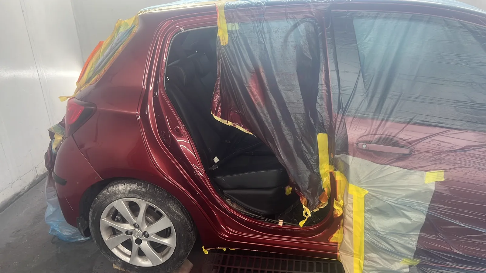 Red hatchback masked with tape and film ready for spraying