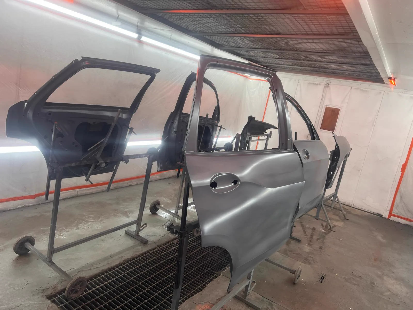 Silver car doors and panels on stands inside the spray booth