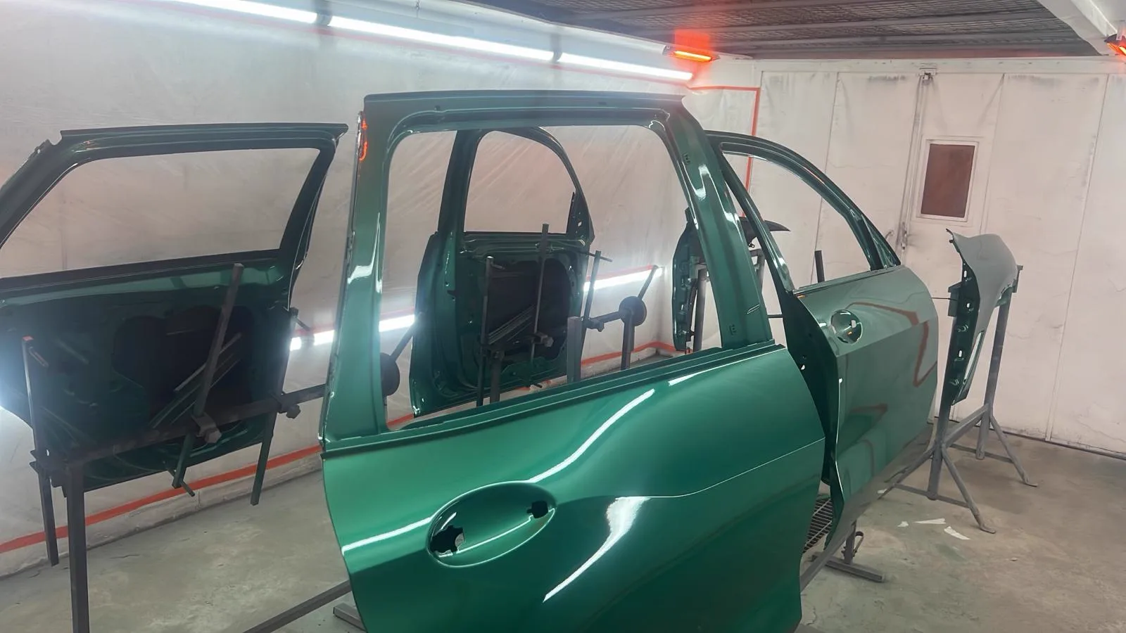 Green car doors and panels freshly refinished in the spray booth